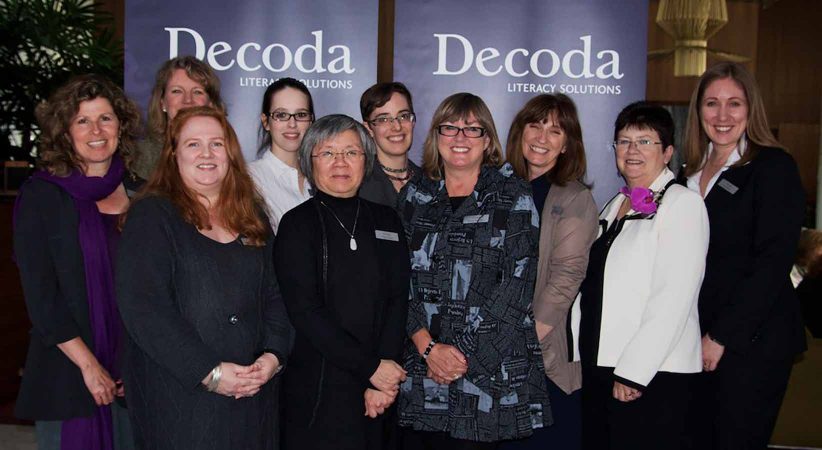Ten women standing in front of a Decoda sign.