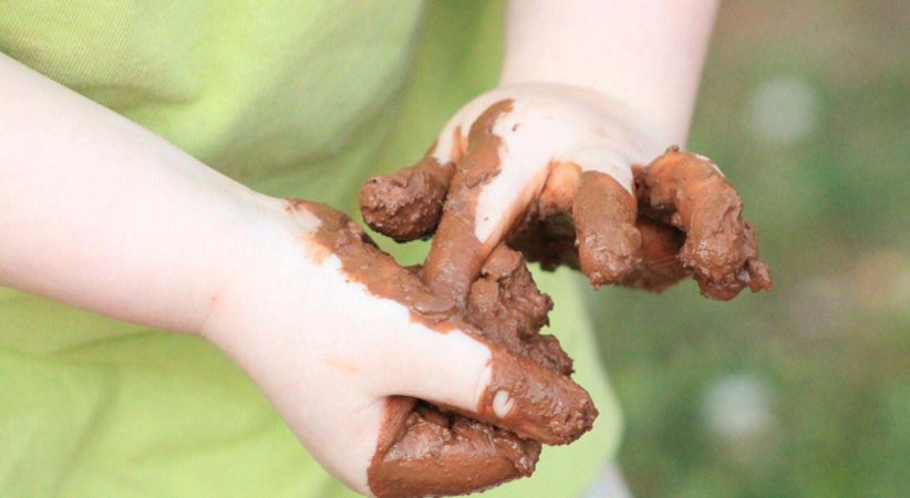 A child's hands play with mud.