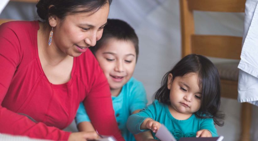 Indigenous woman reads with two children.