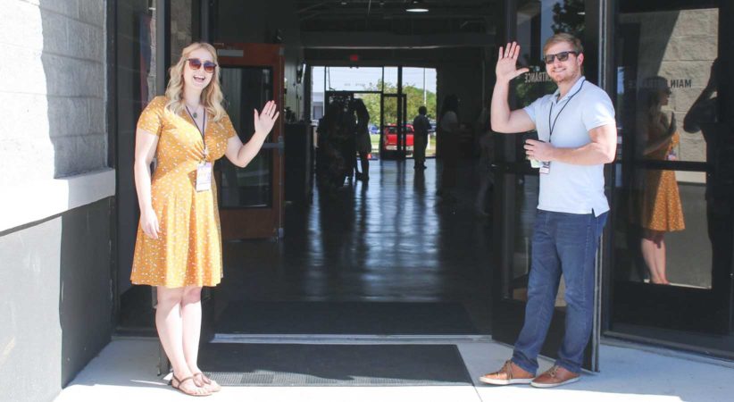 Two people stand at an open door waving