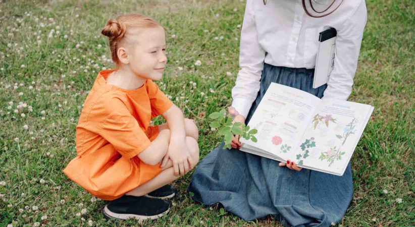 A child looks at a book of plants held by an adult