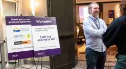 Two people stand to the right of two signs for the Decoda Literacy Conference.