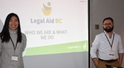 A woman and a man stand in front of a screen which reads Legal Aid BC who we are and what we do.