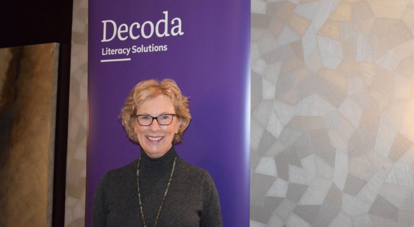 Margaret Sutherland standing in front of a purple banner with the Decoda Literacy Solutions logo displayed.