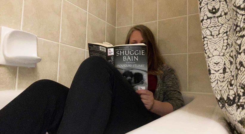 A woman sitting in a bathtub reading Shuggie Bain