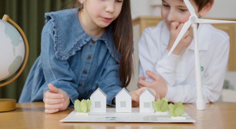 Two children look at an environmental game on a table.