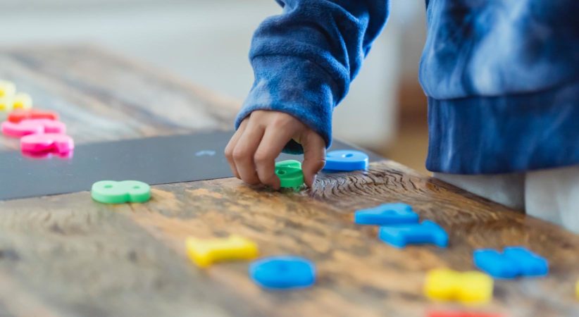 The hand from an unseen child arranges colourful plastic numbers on a table