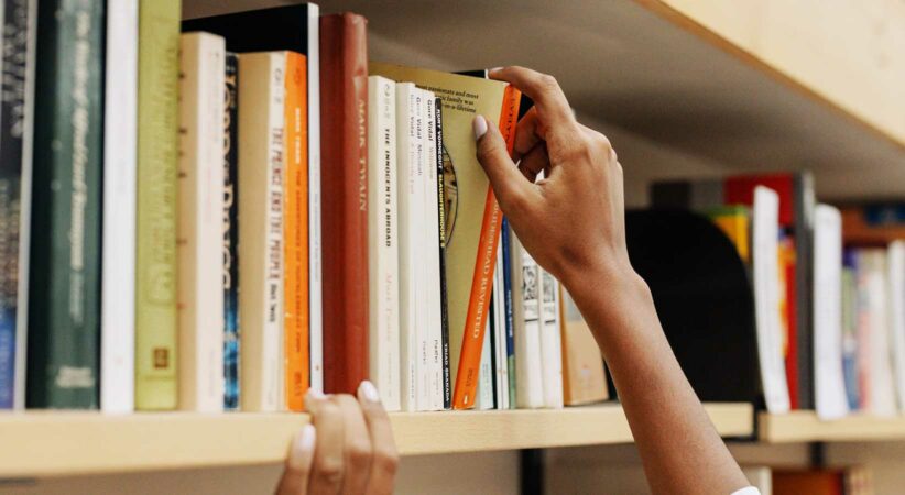 A hand is pulling a book off of a shelf