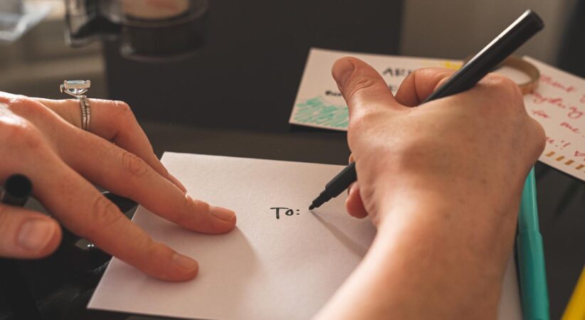 A hand is holding a pen and addressing an envelope.