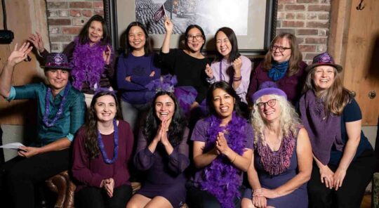 A group of women wearing purple and cheering.
