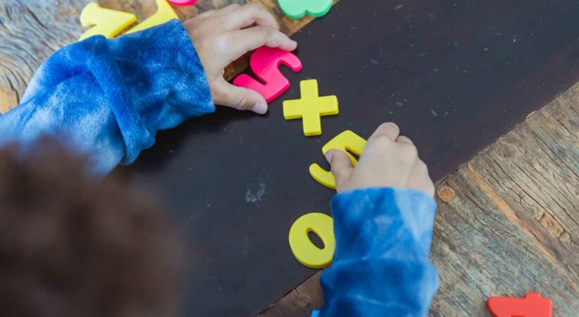 A child's hands are playing with number magnets on a table