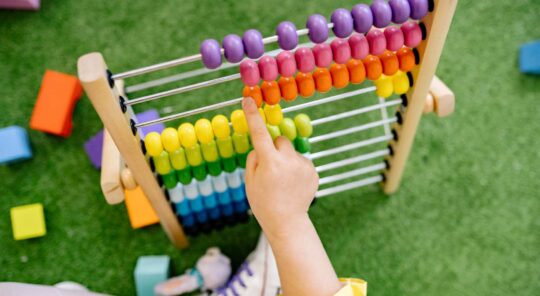 A child's hand is moving beads on an abacus