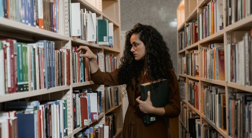 A woman is browsing library shelves and holding a book in one hand