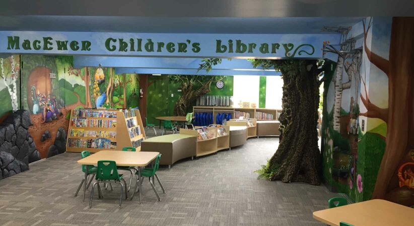 A children's area of a library with shelves, chairs, tables and a tree trunk.