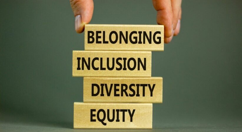 A hand stacks block that read, "belonging, inclusion, diversity and equity."