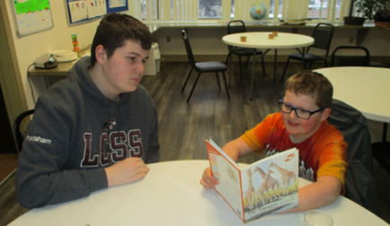 One teen and one child read together while sitting at a table.