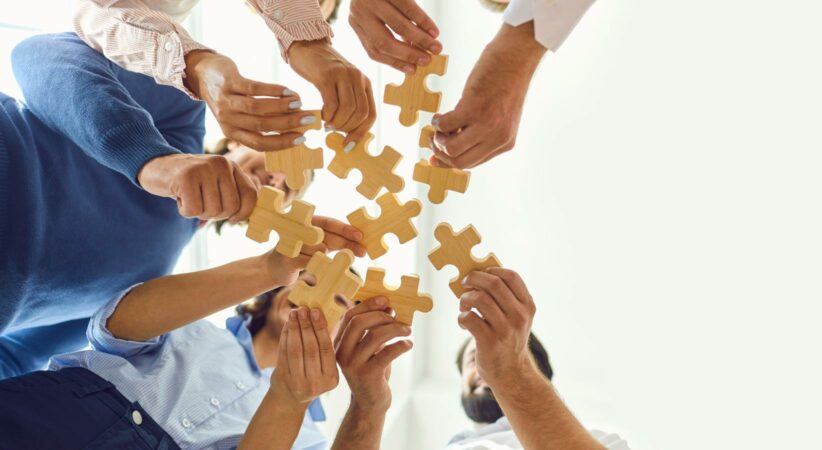 A group of people viewed from below, each holding a wooden jigsaw puzzle piece.