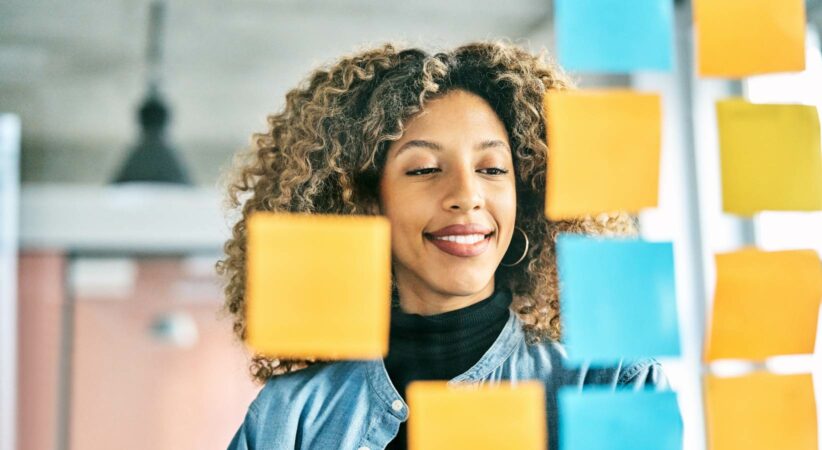 A woman smiles while looking at sticky notes on glass