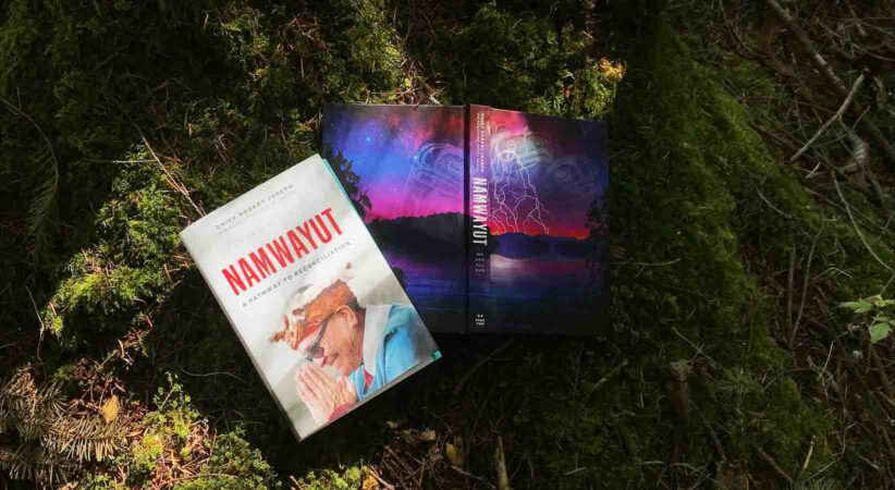 The book and dust cover of Namwayut lying in moss with sunbeams hitting the covers.