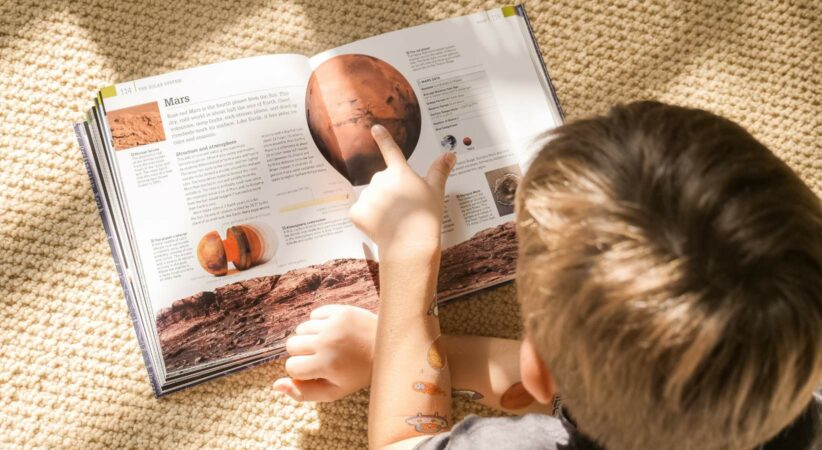 A child reads a book about Mars on the floor.