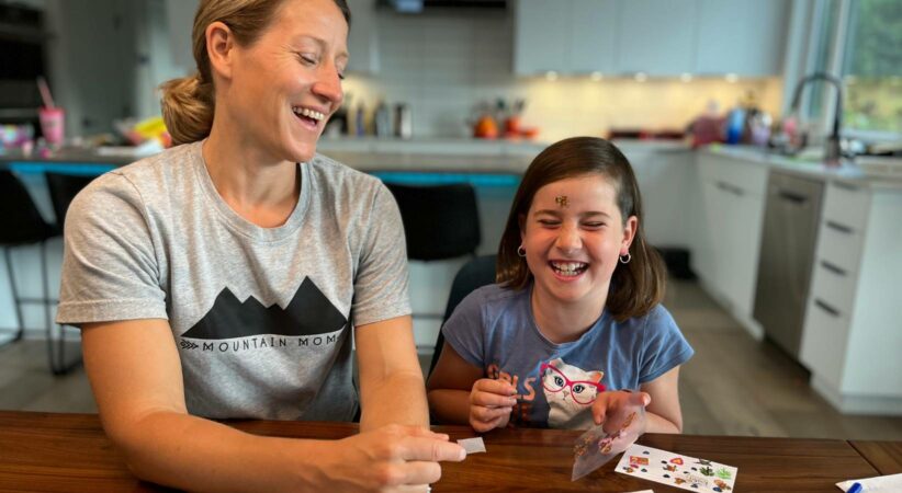 A woman and child sit at a table laughing while using stickers.