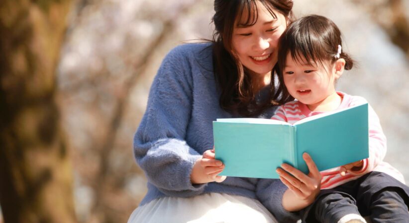 A woman and child reading a book together outdoors.