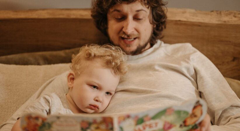 A man is reading to a child in bed.