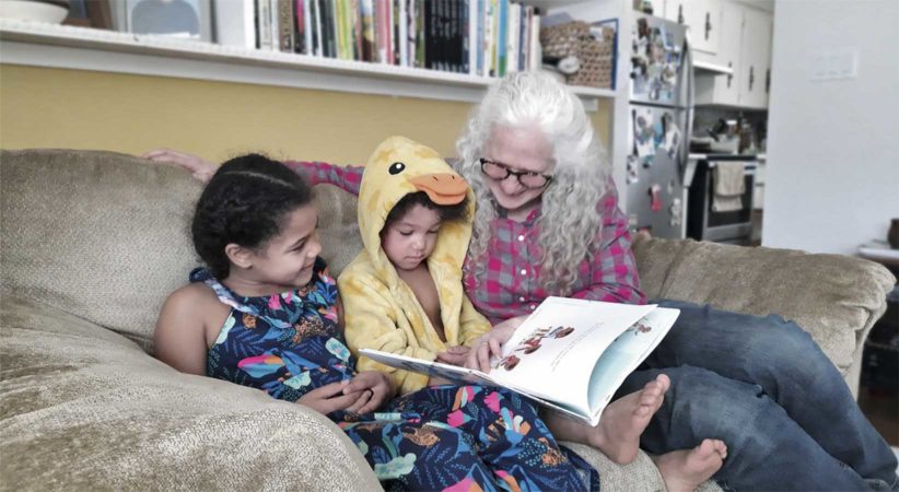 A woman and two children read a picture book on a couch