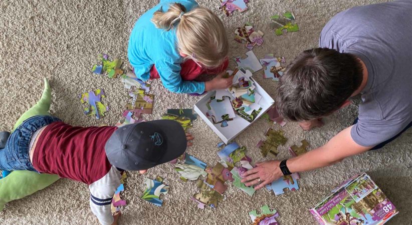 A man and two children work on a puzzle on the floor.