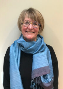 Portrait of a woman standing against a beige background wearing a blue scarf.