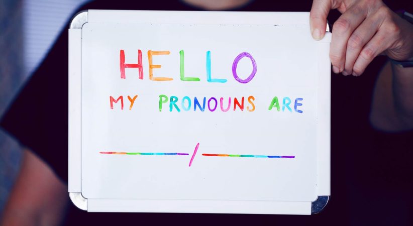Person holding small whiteboard with the words, “Hello my pronouns are...” with blank spaces.