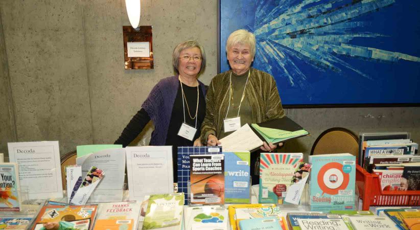 Two women stand behind a table full of books.